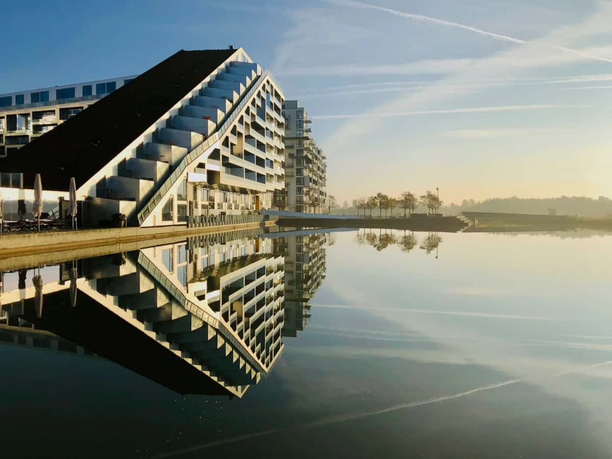 La pointe de la 8 House à Ørestad, sa rampe en pente couverte de végétation et ses balcons blancs en gradins, reflétée dans le canal au lever du jour