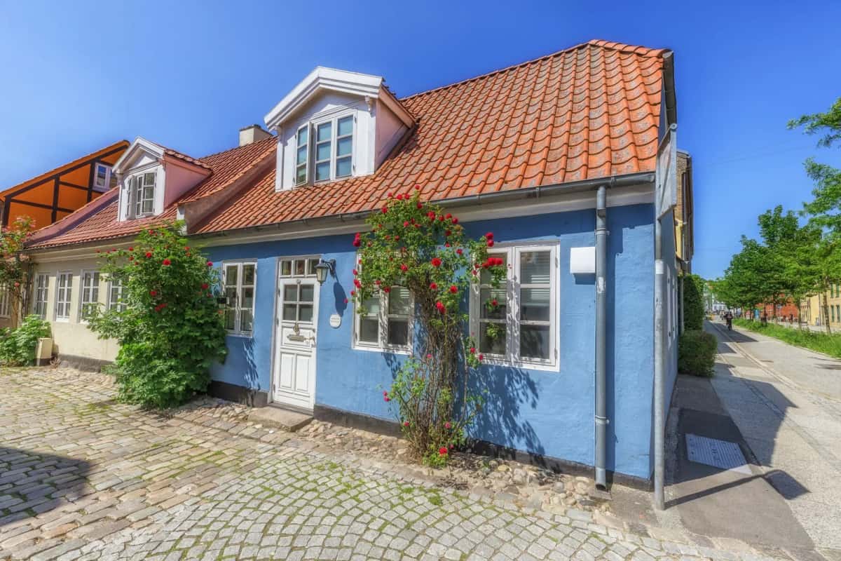 Maison basse aux façades bleues et au toit de tuiles rouges, rosiers grimpants et rue pavée dans le centre d'Aarhus