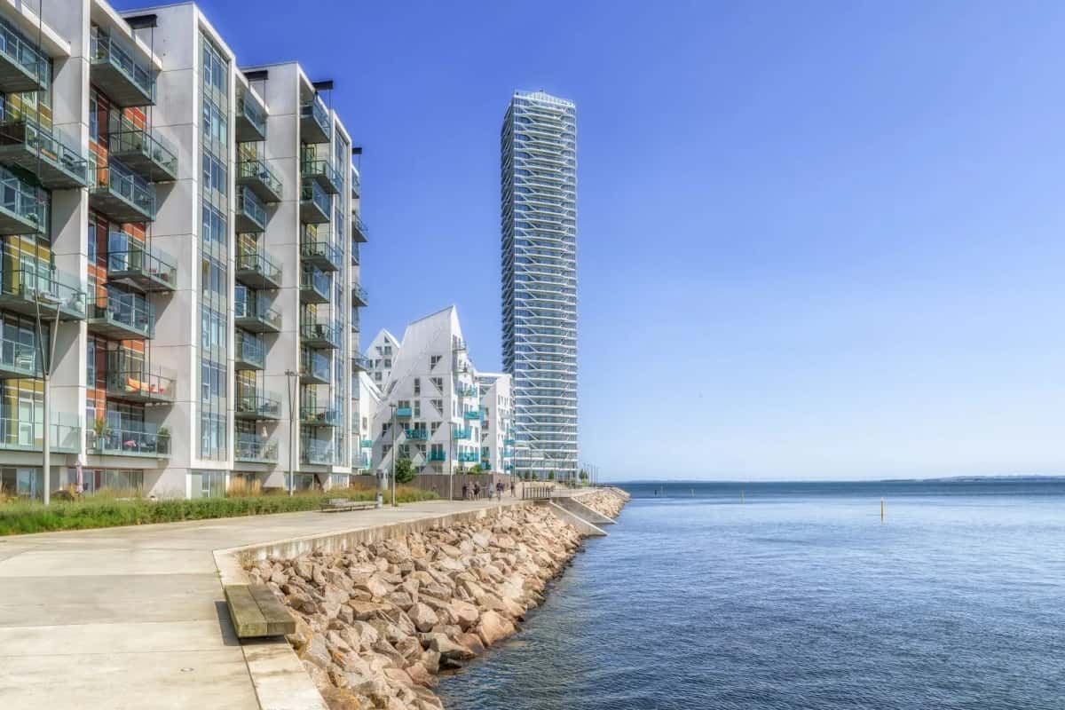 Le quartier d'Aarhus Ø au bord de l'eau : immeubles blancs à balcons en gradins et tour d'habitation élancée, devant un enrochement