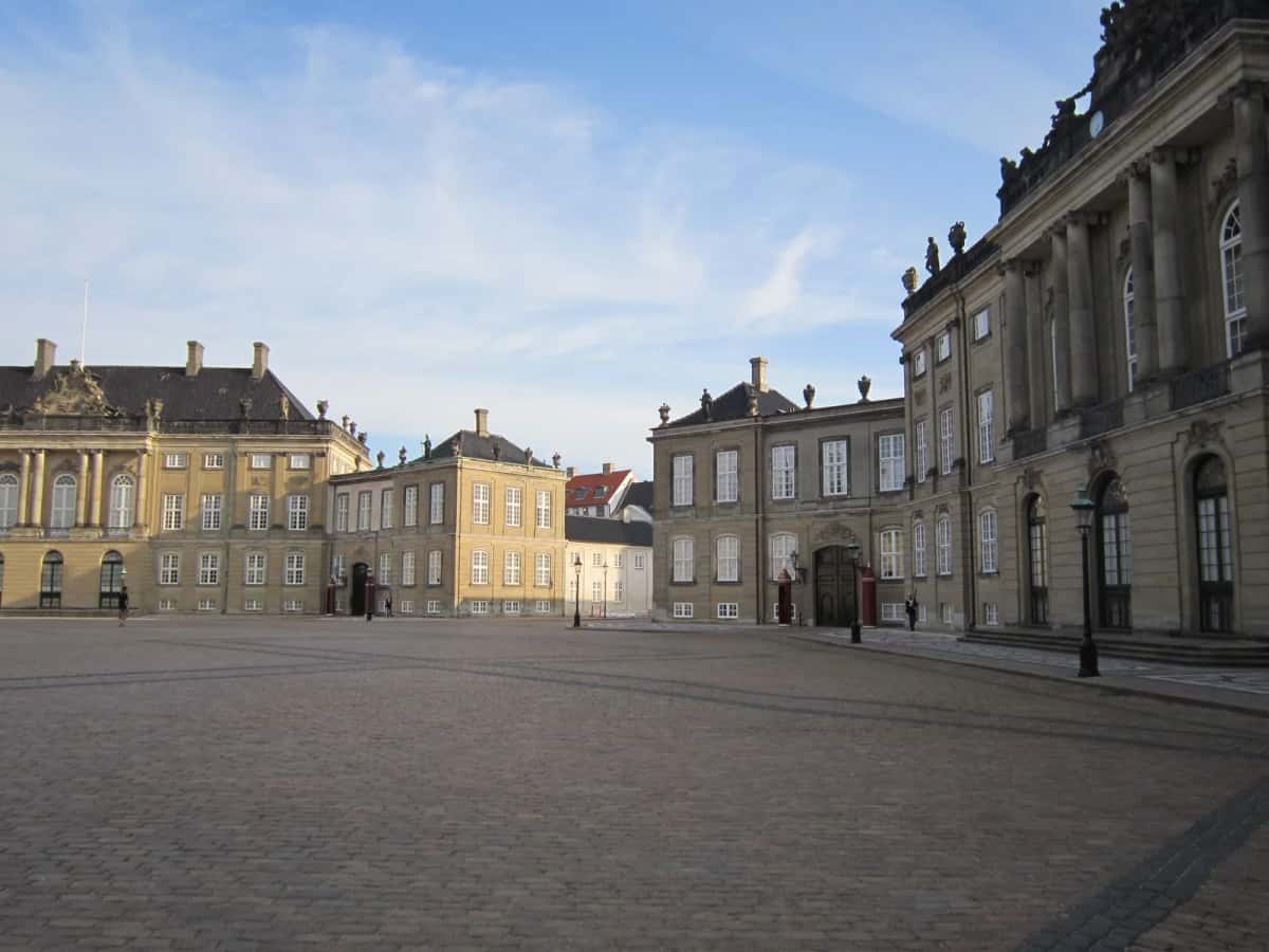 Trois des quatre palais rococo d'Amalienborg autour de la place octogonale pavée, avec une guérite rouge et un garde devant un portail