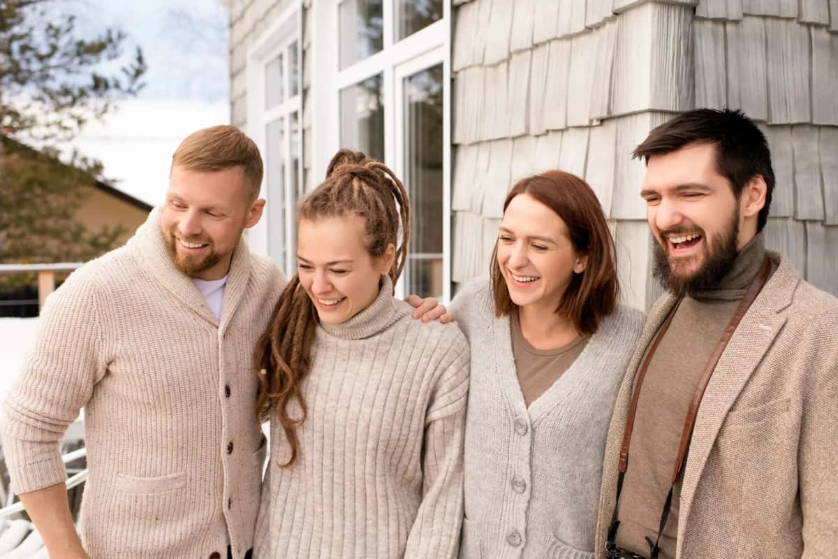 Groupe d'amis danois en pull de laine riant ensemble devant une maison en bois