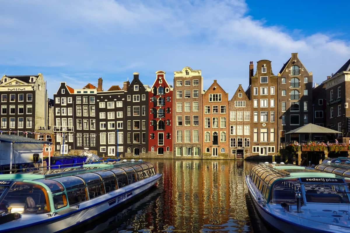 Maisons de canal étroites et penchées le long du Damrak à Amsterdam, bateaux de croisière amarrés au premier plan