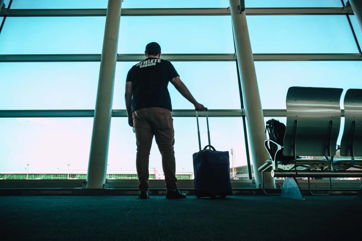 Voyageur de dos avec une valise devant les baies vitrées d'un aéroport, prêt à partir au Danemark