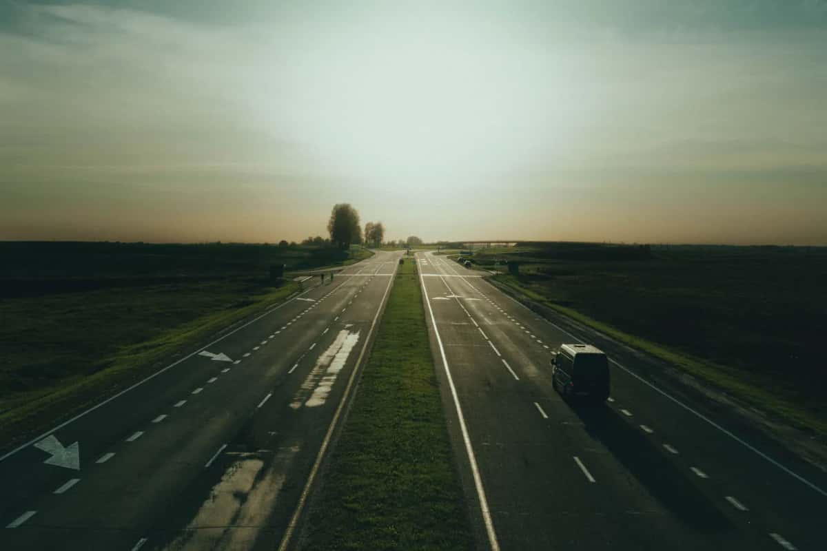 Une autoroute à deux voies presque déserte traversant une plaine agricole, sous un ciel bas de fin de journée