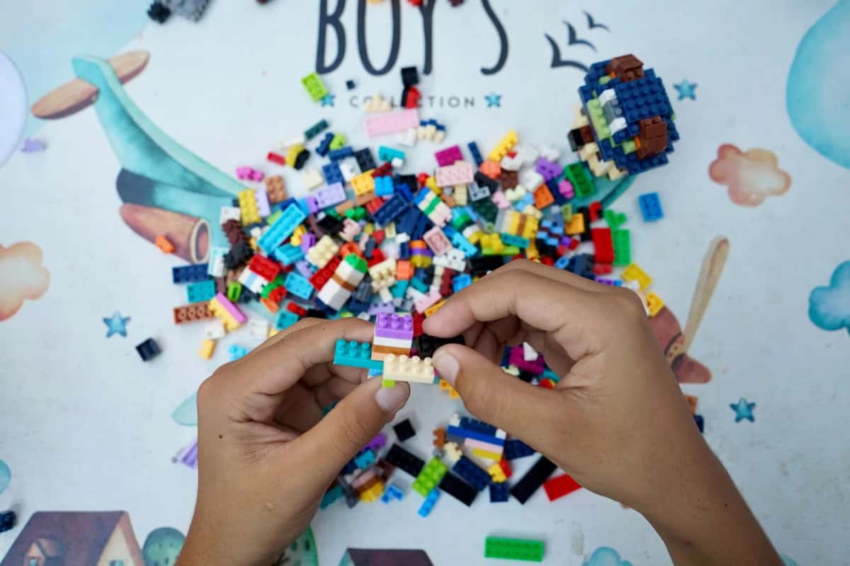 Deux mains assemblant de petites briques LEGO au-dessus d'un tas de briques multicolores étalées sur une table blanche
