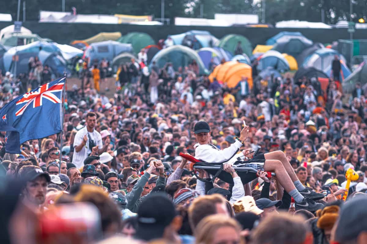 Foule dense au pied d'un camping de festival couvert de tentes multicolores, quelques drapeaux brandis au-dessus des têtes