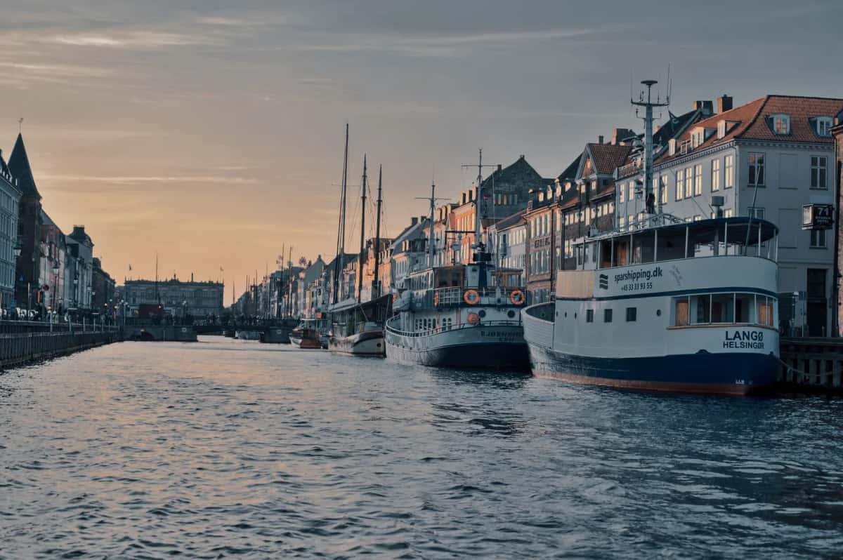 Canal urbain au crépuscule, vieux bateaux et péniches amarrés des deux côtés devant des façades anciennes
