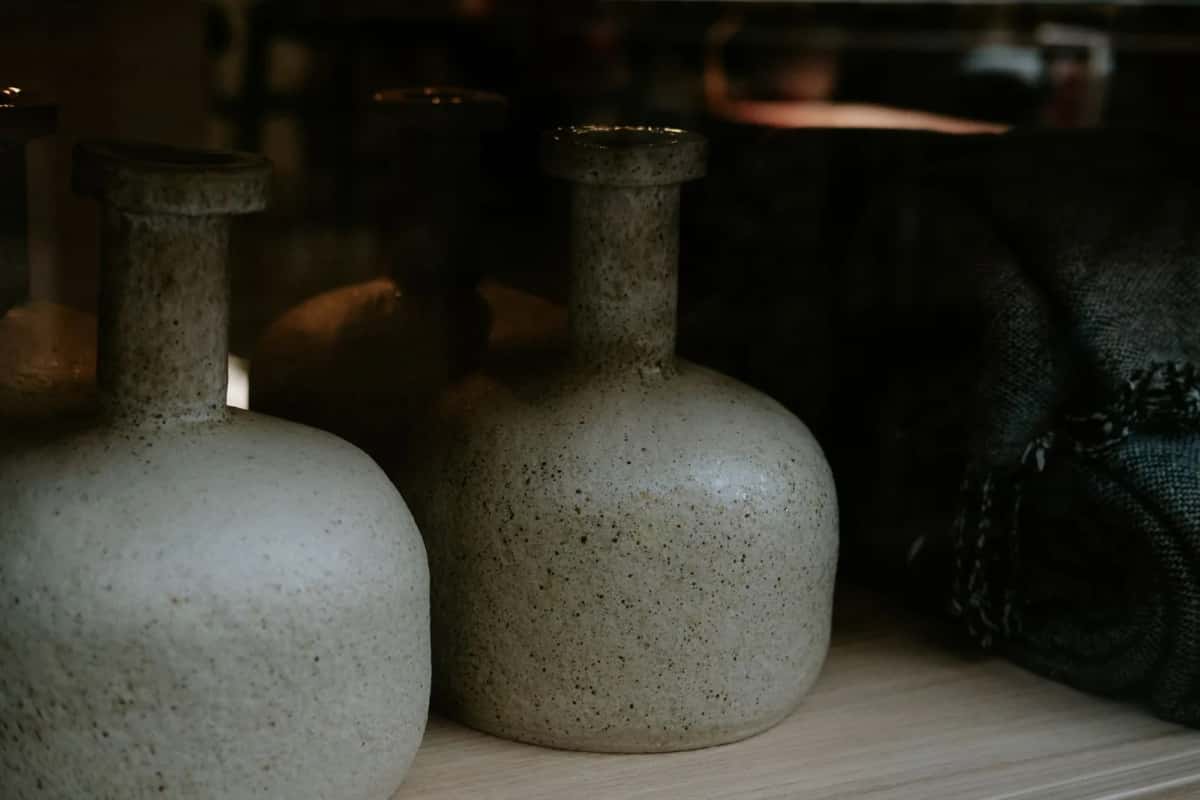 Trois vases en grès émaillé aux teintes gris-vert, alignés sur une étagère dans une lumière basse
