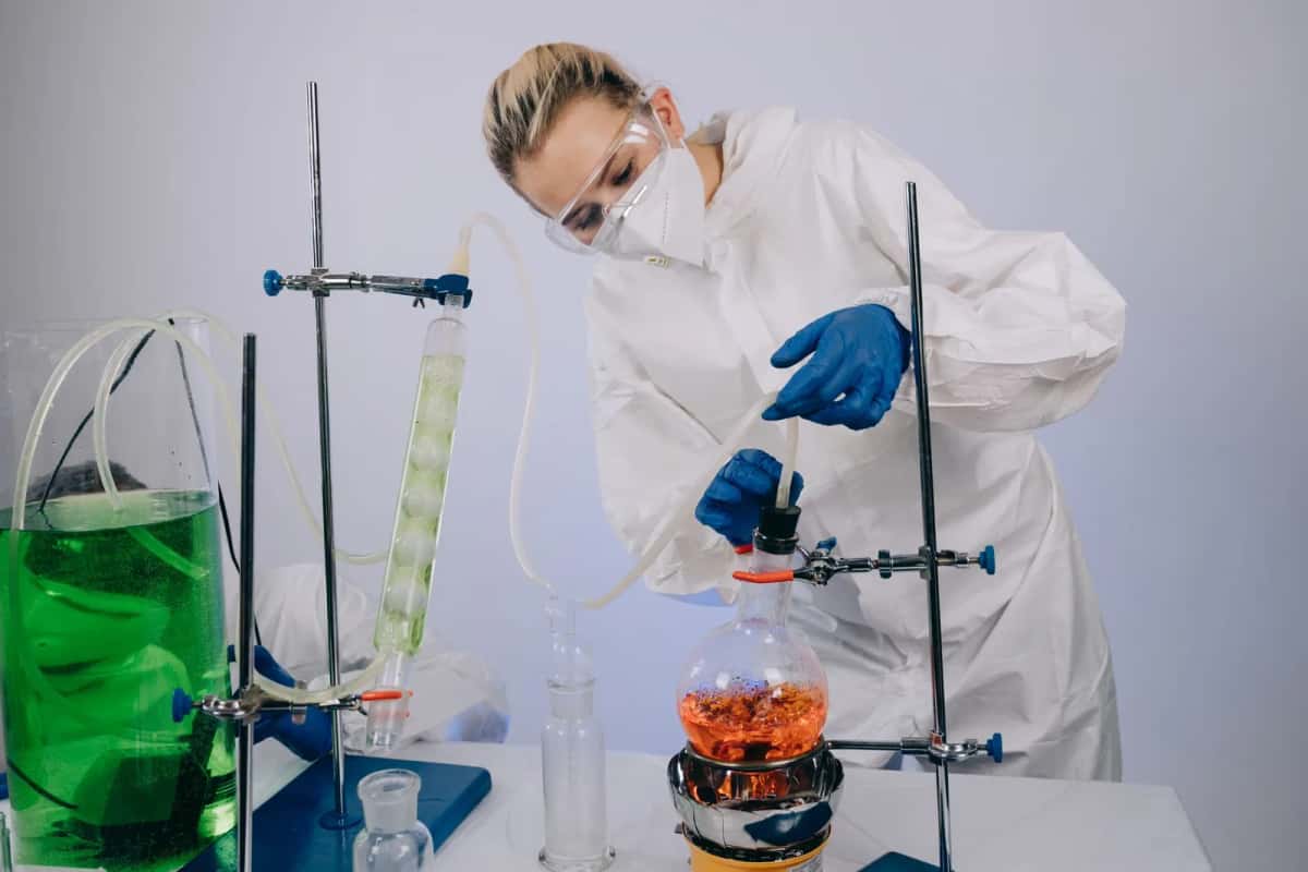 Chercheuse en blouse et gants manipulant de la verrerie et un liquide coloré sur une paillasse de laboratoire