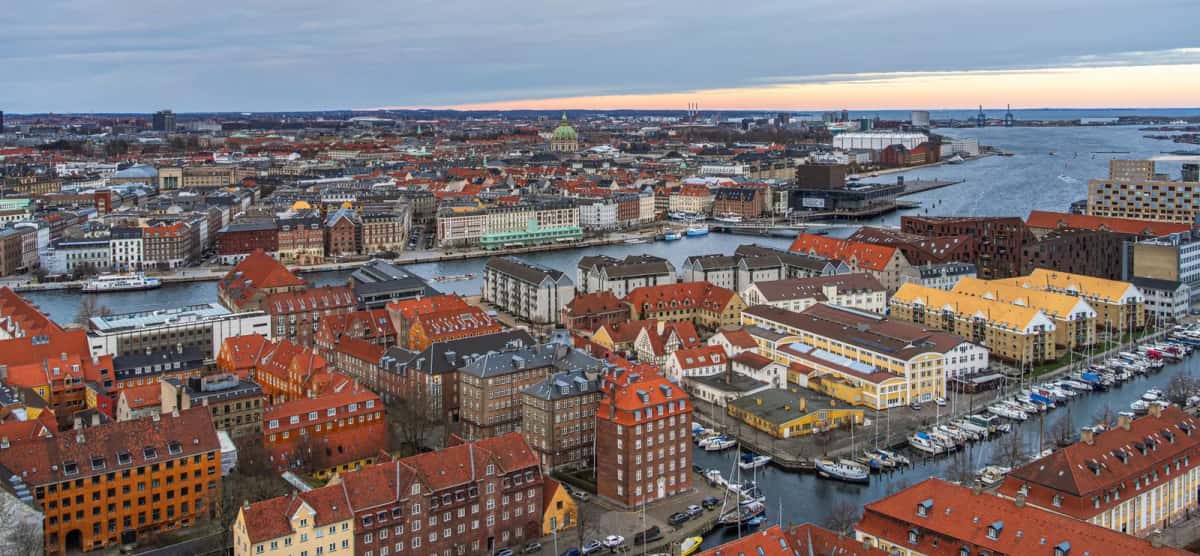Vue plongeante sur Christianshavn et le port intérieur de Copenhague au crépuscule, toits de tuiles rouges, canal bordé de bateaux et dôme vert de l'église de Marbre au loin