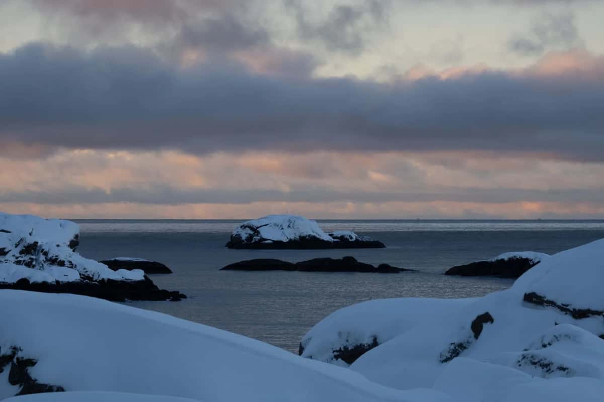 Rochers couverts de neige au bord d'une mer grise et calme, sous un ciel rose de fin de journée