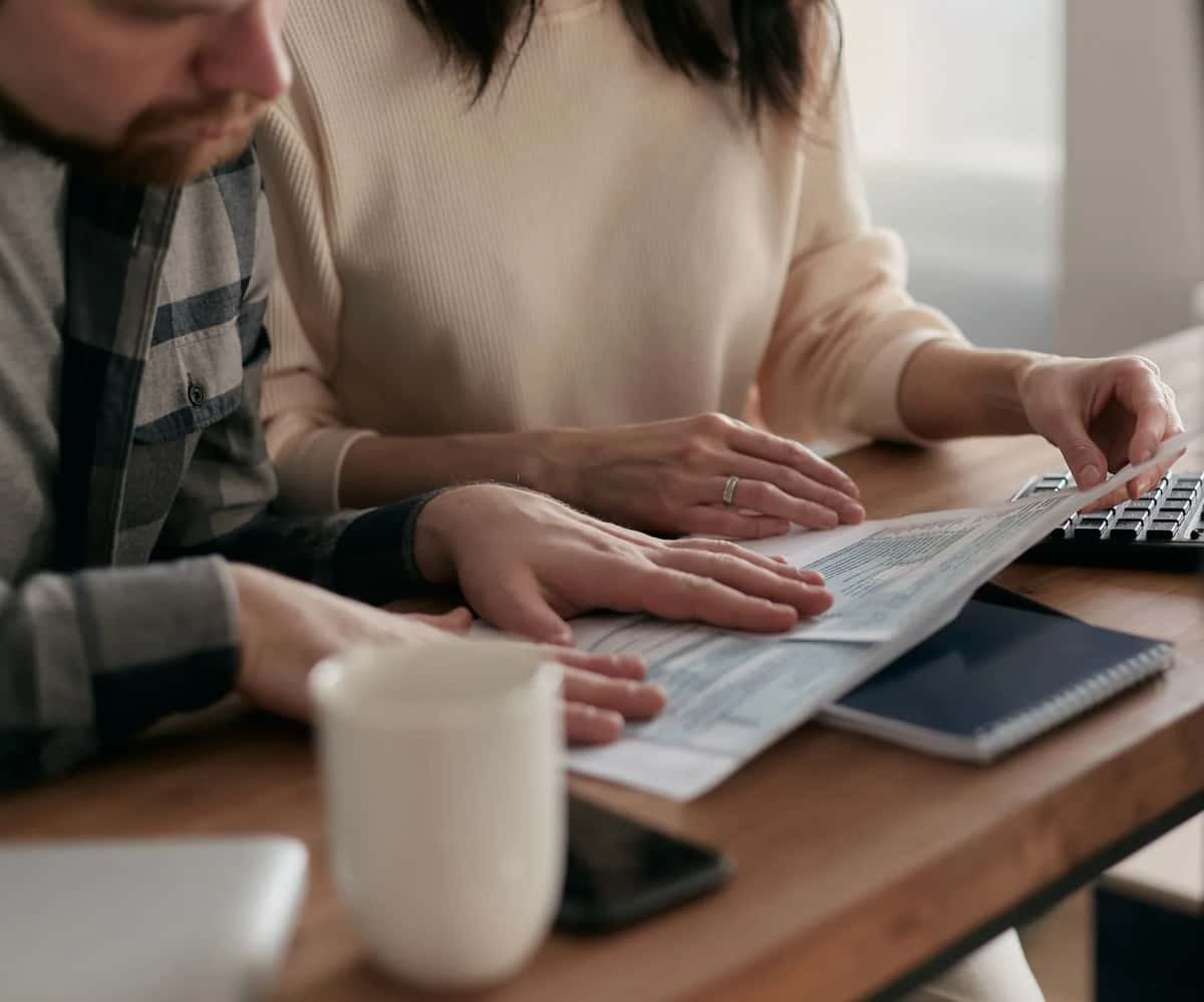 Deux personnes penchées sur un formulaire imprimé posé sur une table en bois, une calculatrice et un carnet à côté d'une tasse