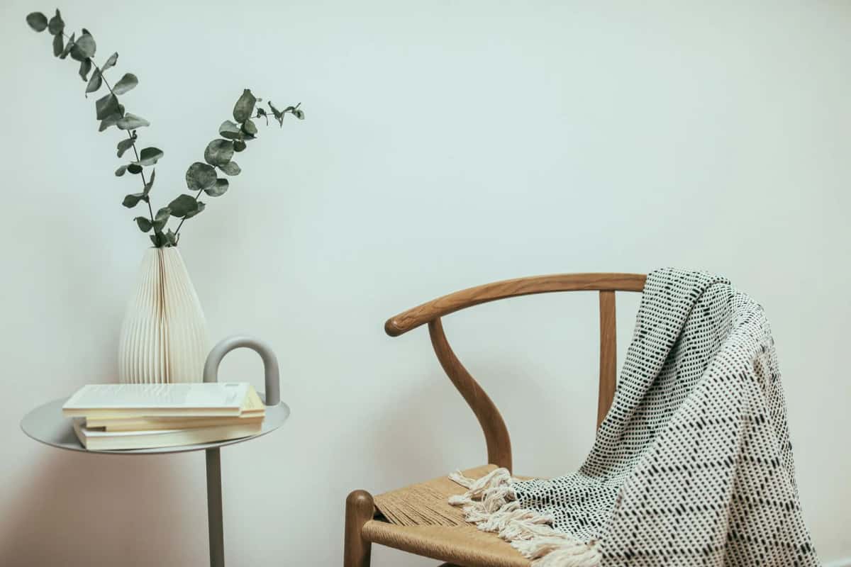 Chaise en bois danoise avec plaid tricoté, vase et pile de livres, ambiance hygge et design scandinave