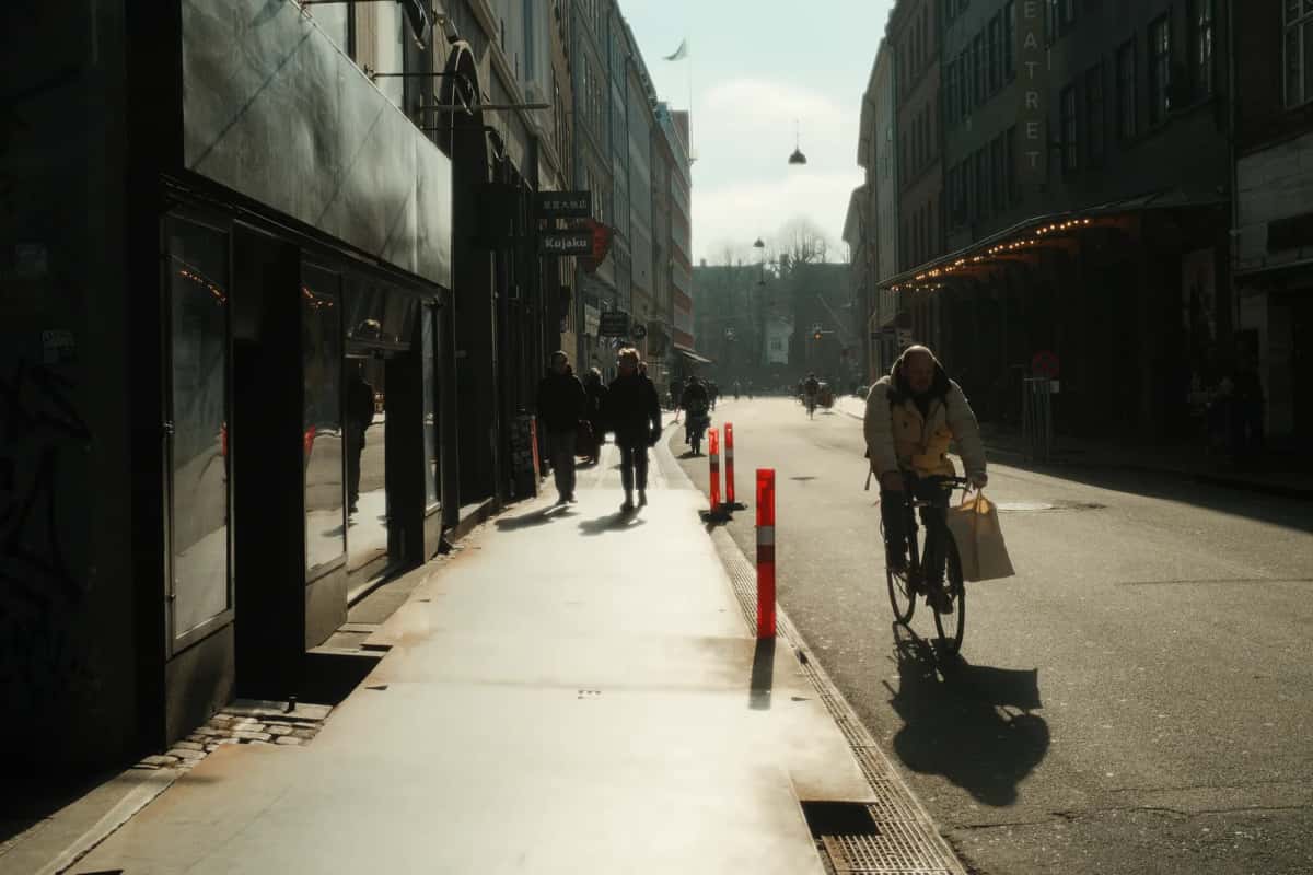 Cycliste de dos, sacoche au guidon, dans une rue au petit matin où le soleil rasant projette une longue ombre