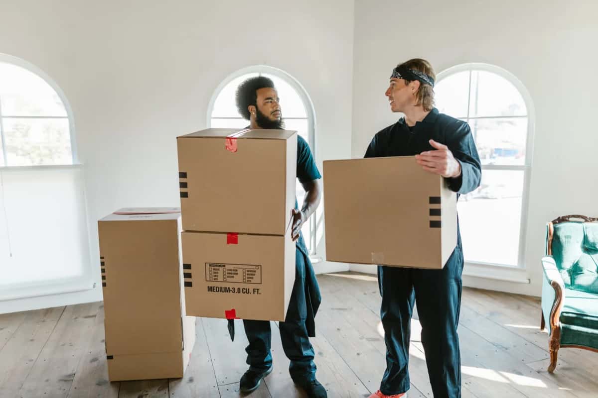 Deux déménageurs portant des cartons étiquetés dans un appartement vide