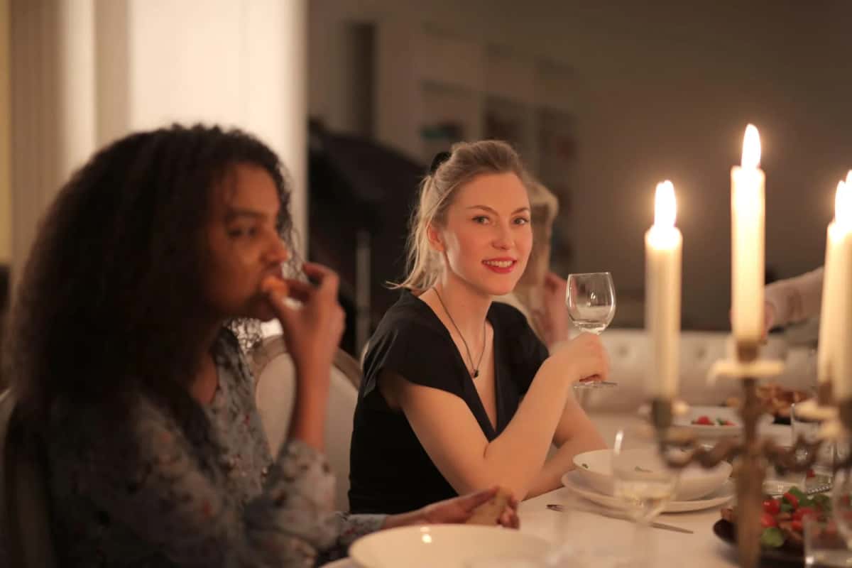 Deux convives attablées à la lueur de grandes bougies, verres de vin à la main, en pleine conversation
