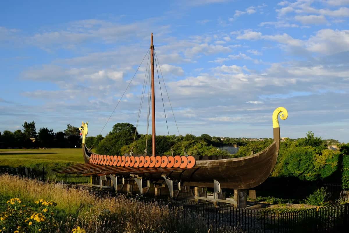 Réplique de navire viking posée sur un ber en plein air, coque en bois à bordé à clin et rangée de boucliers ronds accrochés le long du plat-bord