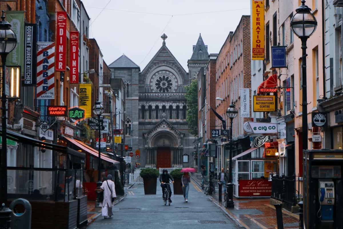 Rue commerçante de Dublin sous la pluie, enseignes de boutiques et façade d'une église en pierre au fond