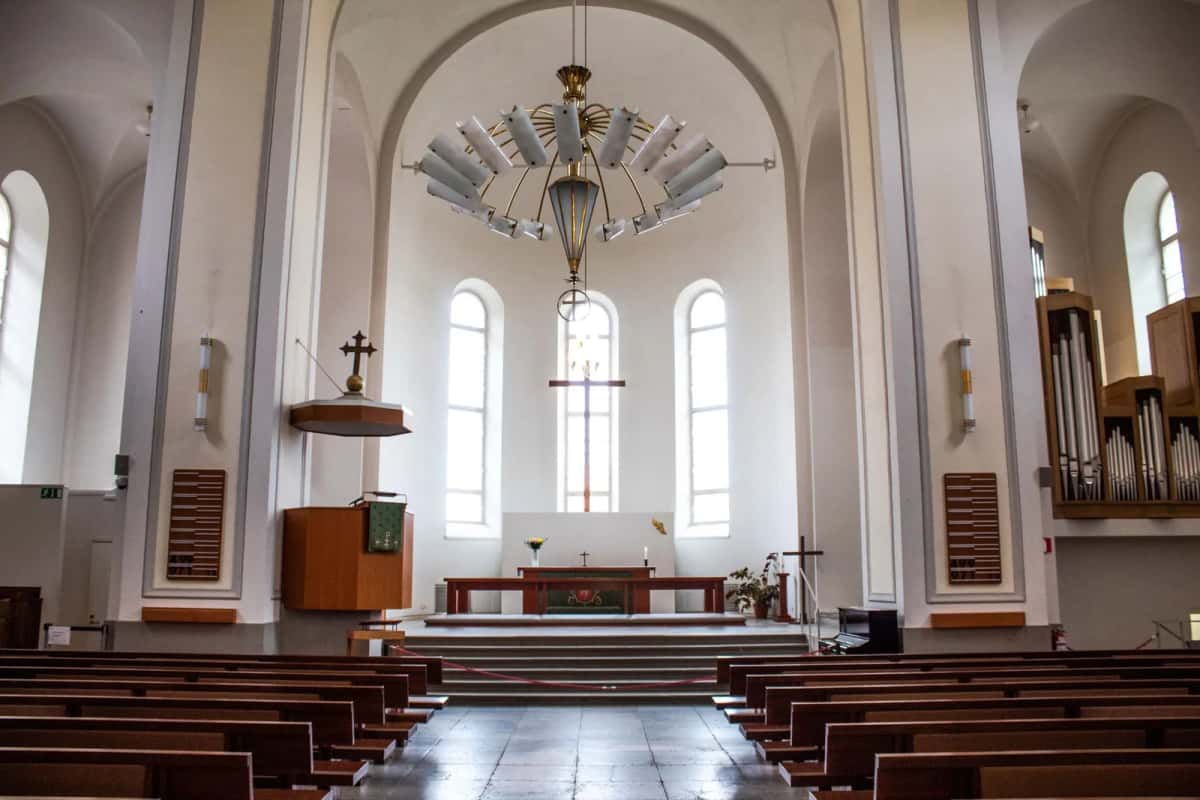 Nef d'une église protestante aux murs blancs et à la voûte claire, rangées de bancs en bois, autel et lustre au centre