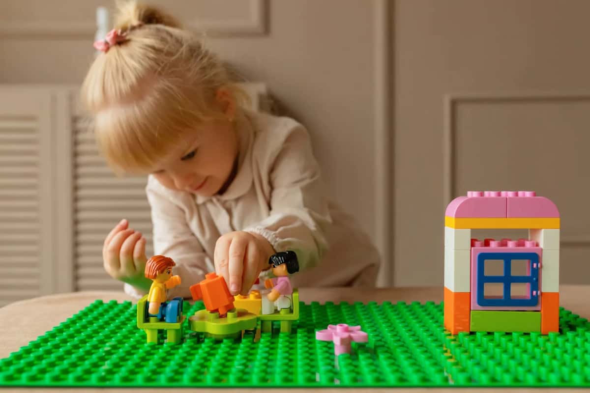 Une petite fille assemblant des briques DUPLO colorées sur une plaque de base verte, assise à une table