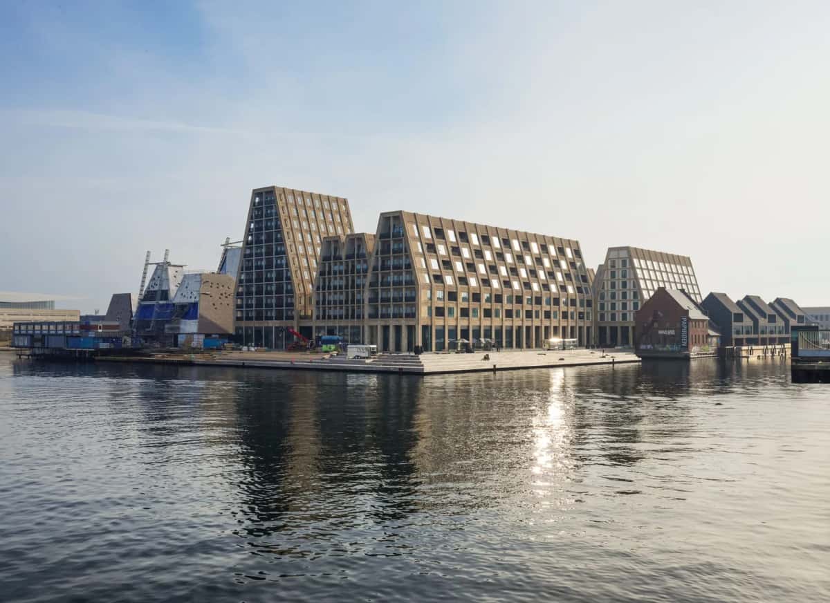Long bâtiment contemporain en brique claire aux toits en pignons dentelés, posé au bord de l'eau dans un ancien bassin portuaire