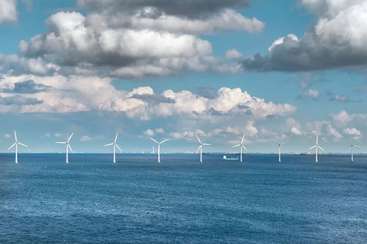 Alignement d'éoliennes offshore posées en pleine mer au Danemark, cargo passant entre les mâts et côte basse à l'horizon