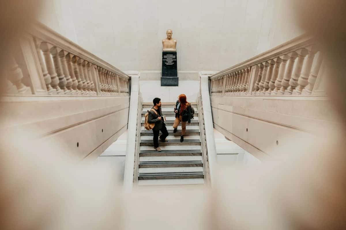 Deux étudiants sac au dos montant un escalier monumental d'université, livres en main