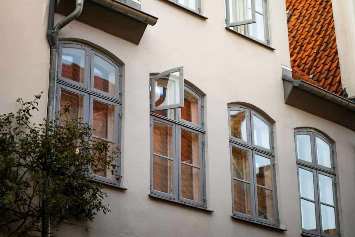 Façade claire d'un immeuble ancien, hautes fenêtres cintrées à croisillons blancs et gouttière de zinc sous un toit de tuiles