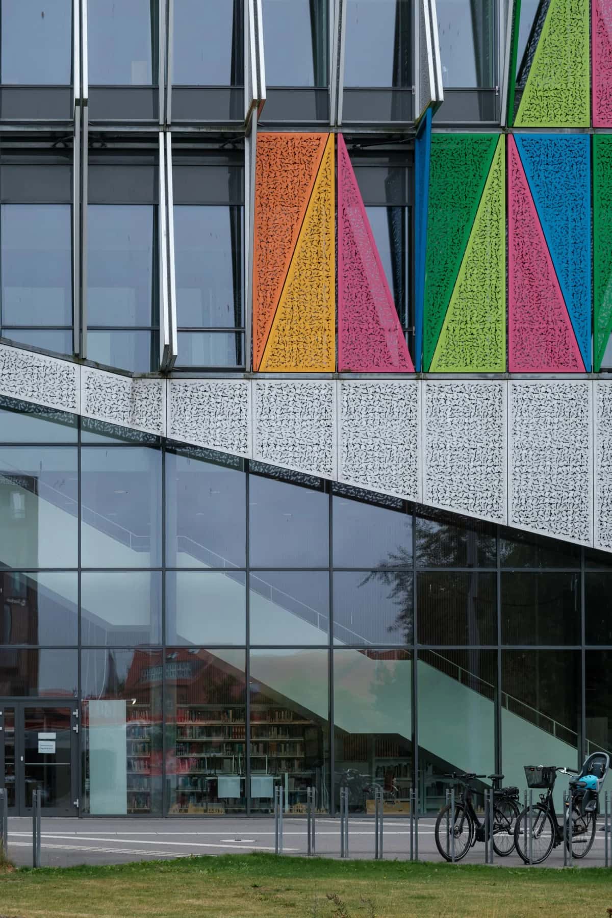 Façade vitrée d'un bâtiment contemporain habillée de panneaux triangulaires jaunes, roses et verts