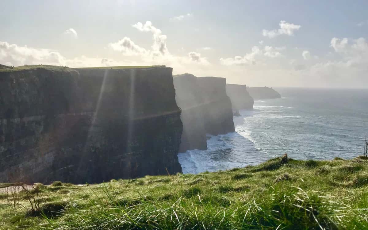 Hautes falaises stratifiées plongeant dans l'Atlantique, herbe rase battue par le vent au premier plan