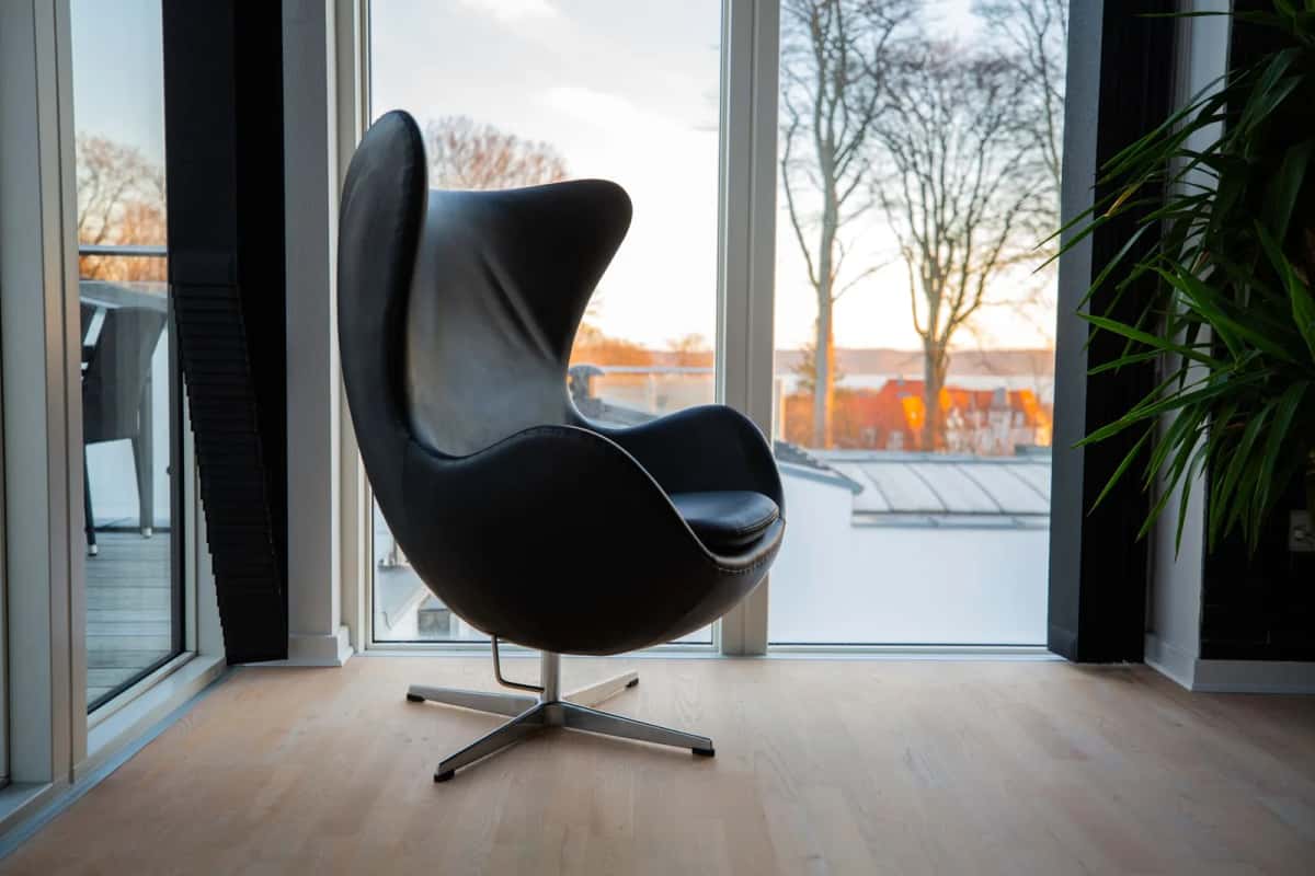 Un fauteuil Egg noir en cuir devant une baie vitrée donnant sur des arbres nus, dans une pièce au parquet clair