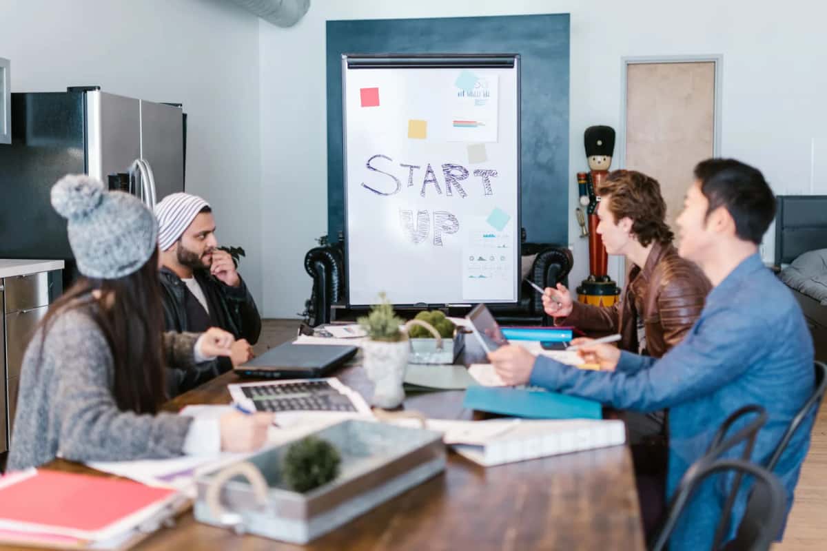 Équipe de fondateurs de startup en réunion autour d'une table de travail avec tableau blanc