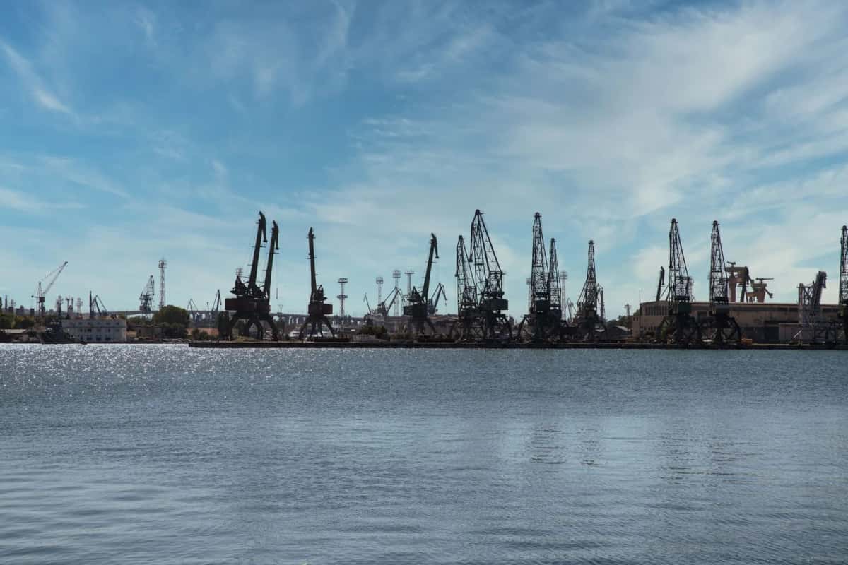 Rangée de grues portuaires en silhouette au bout d'un quai, au-dessus d'un plan d'eau calme
