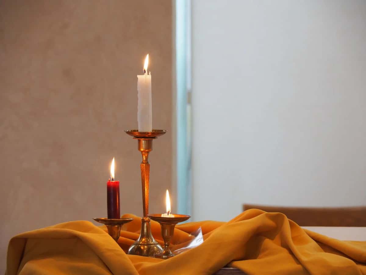 Bougies allumées dans des bougeoirs en laiton sur une nappe chaude, ambiance hygge danoise