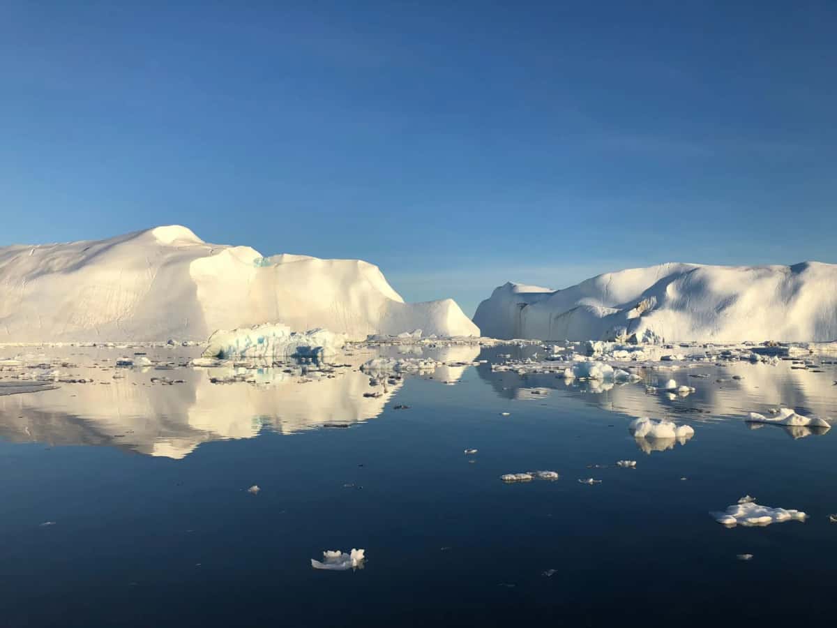 Champ d'icebergs plats et de blocs de glace dérivant sur une mer arctique parfaitement lisse, sous un ciel voilé