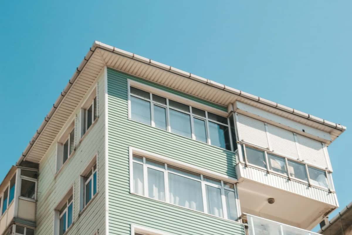 Angle d'un petit immeuble d'habitation à façade claire, balcons vitrés et fenêtres blanches, vu en contre-plongée