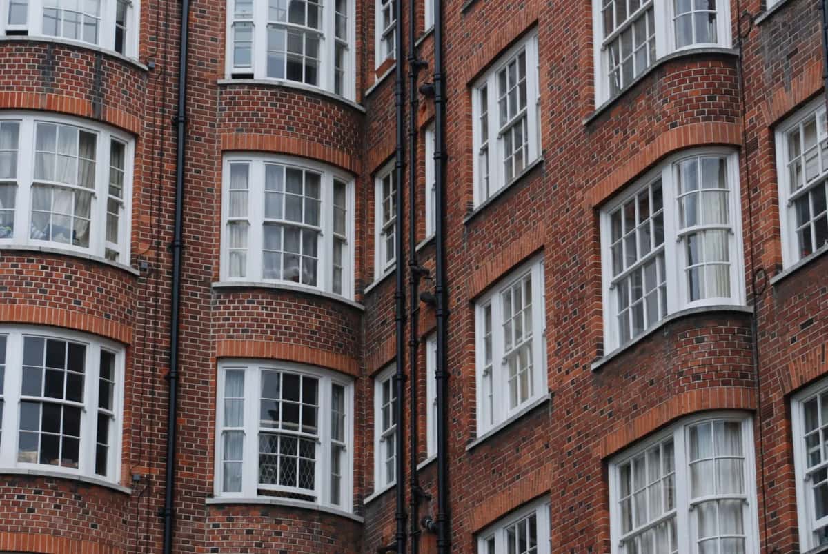Immeuble d'habitation en brique rouge sombre à l'angle de deux rues, bow-windows blancs superposés sur cinq niveaux