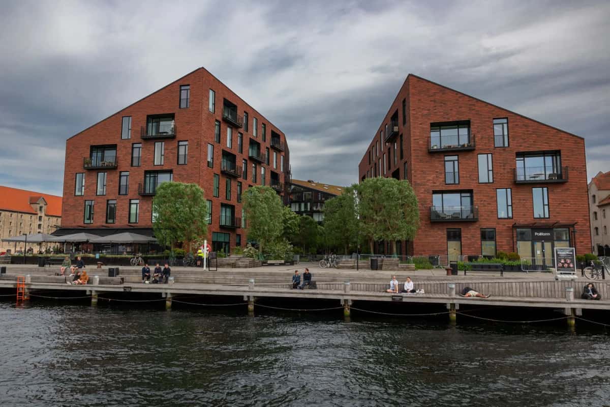 Deux immeubles d'habitation contemporains en brique rouge, aux toits en pente, bordant un quai en bois au bord d'un canal