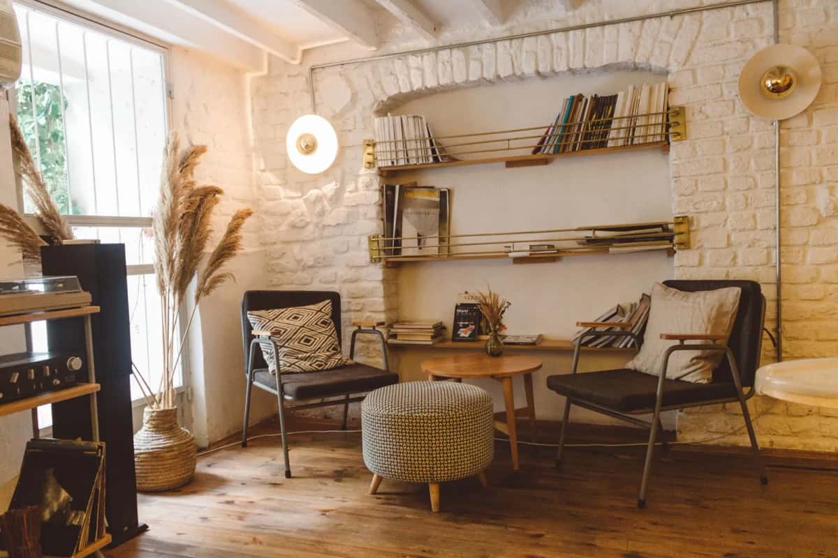 Salon scandinave clair avec deux fauteuils, une table basse, des étagères de livres et des herbes séchées devant une fenêtre