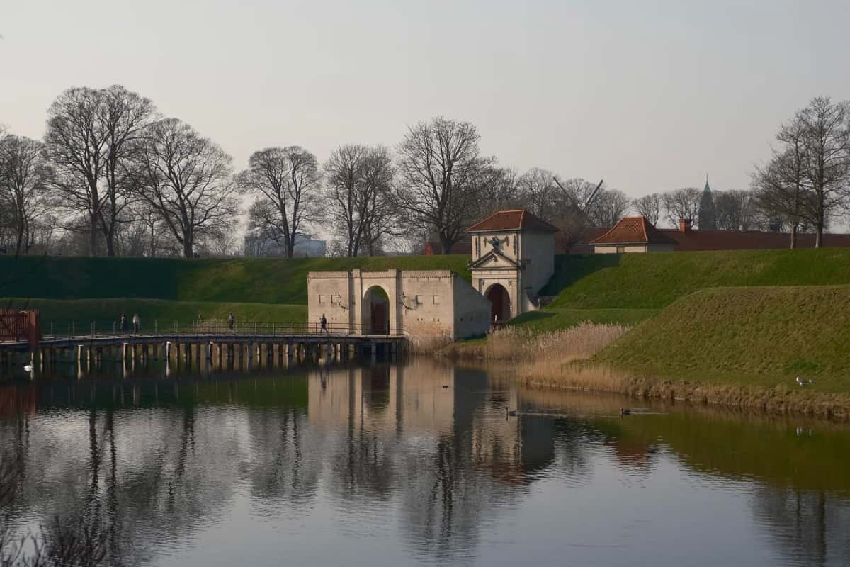 Porte de la citadelle de Kastellet à Copenhague vue depuis l'autre rive des douves, talus gazonnés et arbres nus reflétés dans l'eau