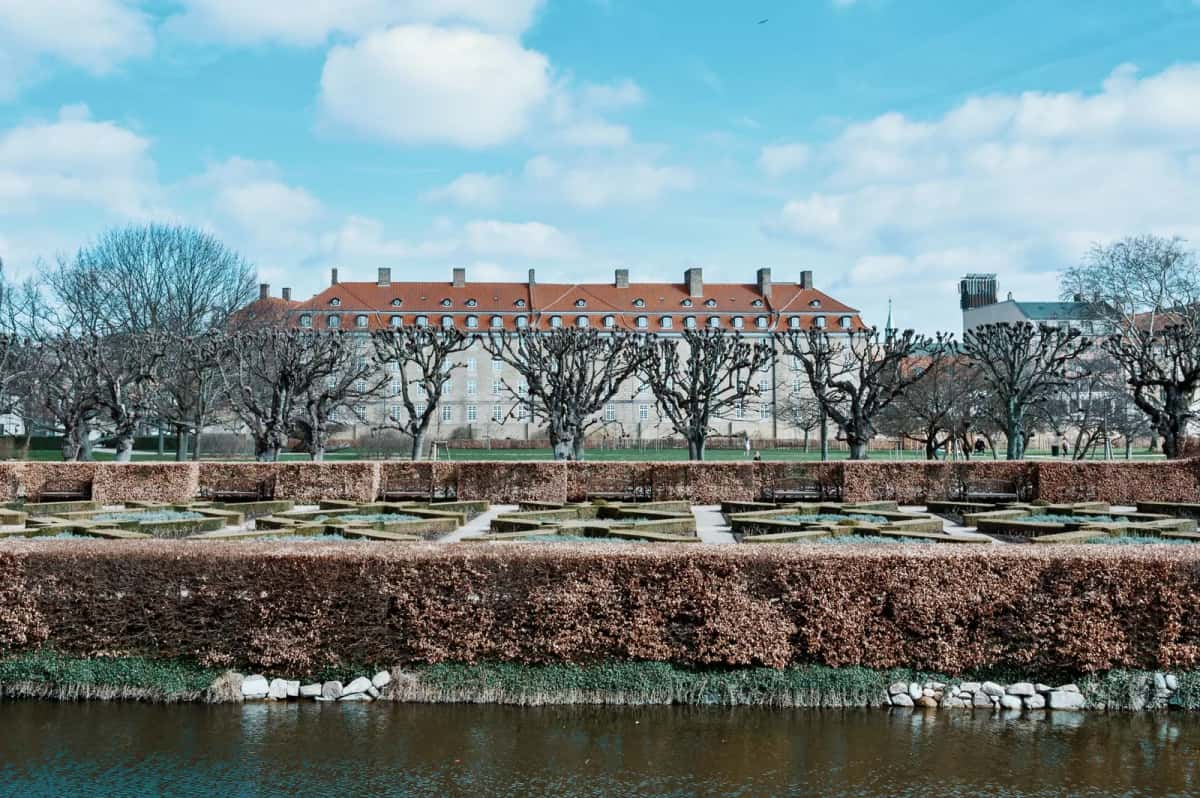 Kongens Have en hiver à Copenhague, parterres géométriques taillés, arbres dénudés alignés le long du canal et longue façade claire au fond