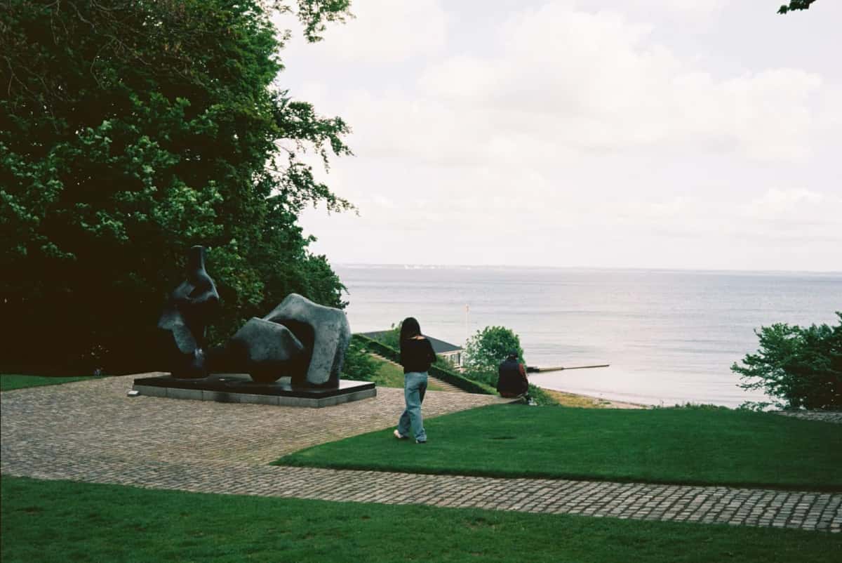 Parc de sculptures du Louisiana à Humlebæk, bronze massif posé sur une pelouse en pente qui descend vers l'Øresund, une visiteuse marchant à côté