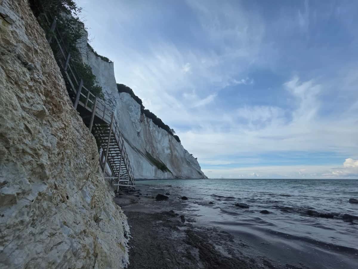 Escalier de bois accroché à la paroi de craie blanche de Møns Klint, descendant jusqu'à une plage de galets battue par la Baltique
