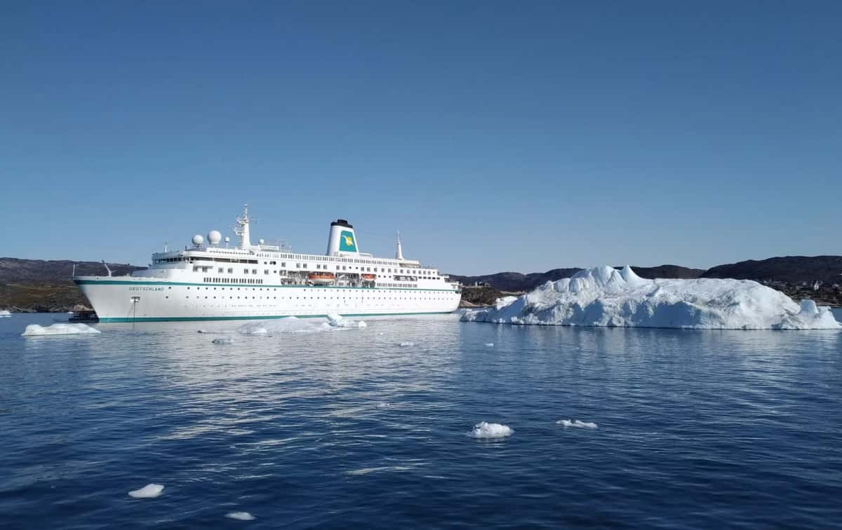 Navire de croisière blanc naviguant au milieu d'icebergs, le long d'une côte arctique dénudée