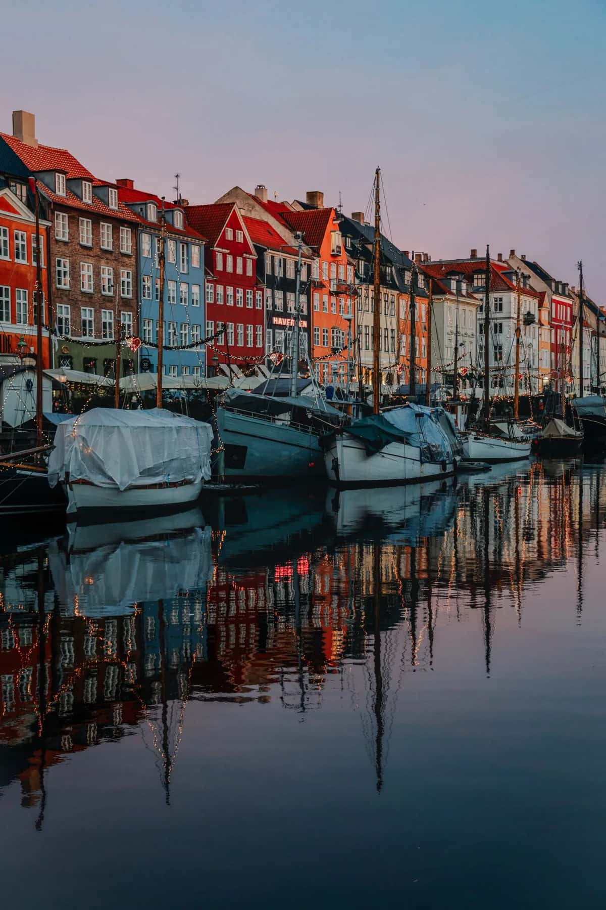 Le canal de Nyhavn à Copenhague au petit matin, façades colorées et vieux voiliers en bois amarrés, guirlandes lumineuses reflétées dans l'eau