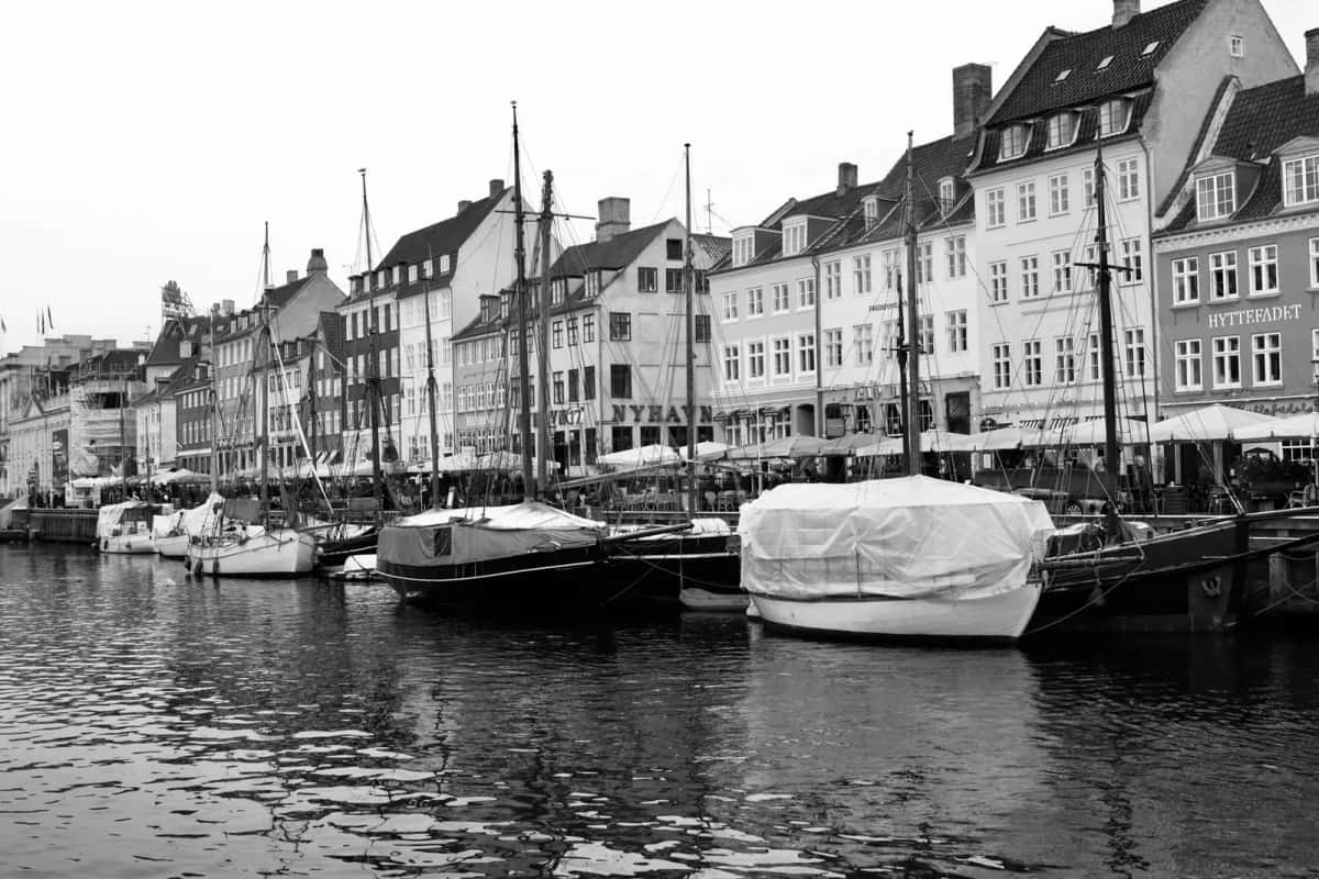 Quai de Nyhavn en noir et blanc : rangée continue de maisons à pignon, terrasses sous parasols et bateaux de bois amarrés le long du canal