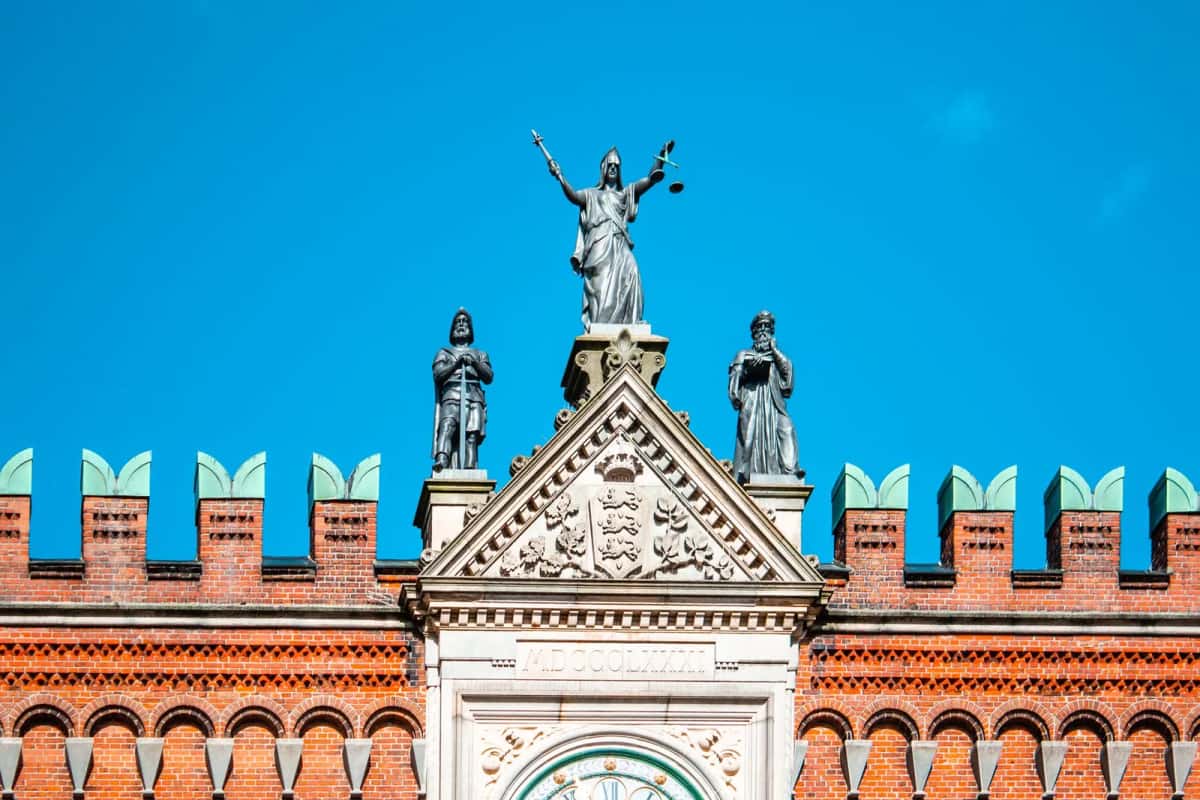 Pignon en brique rouge du palais de justice d'Odense, arcatures, créneaux et statue de la Justice au sommet sur fond de ciel bleu