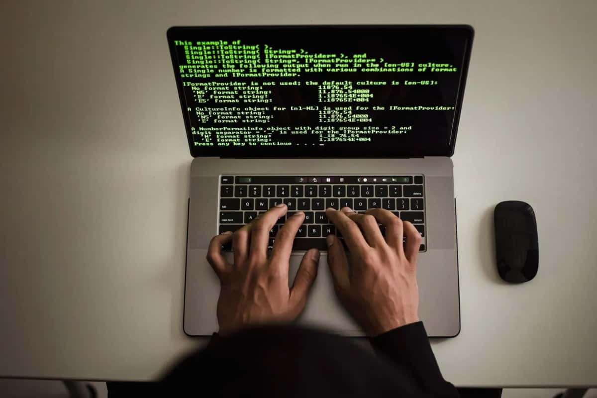 Vue de dessus des mains d'une personne tapant sur un ordinateur portable affichant des lignes de code sur fond noir