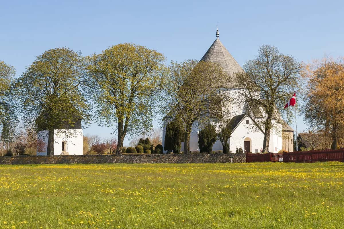 L'église ronde d'Østerlars, ses murs blanchis à la chaux, son toit conique et ses contreforts, au milieu d'un pré fleuri