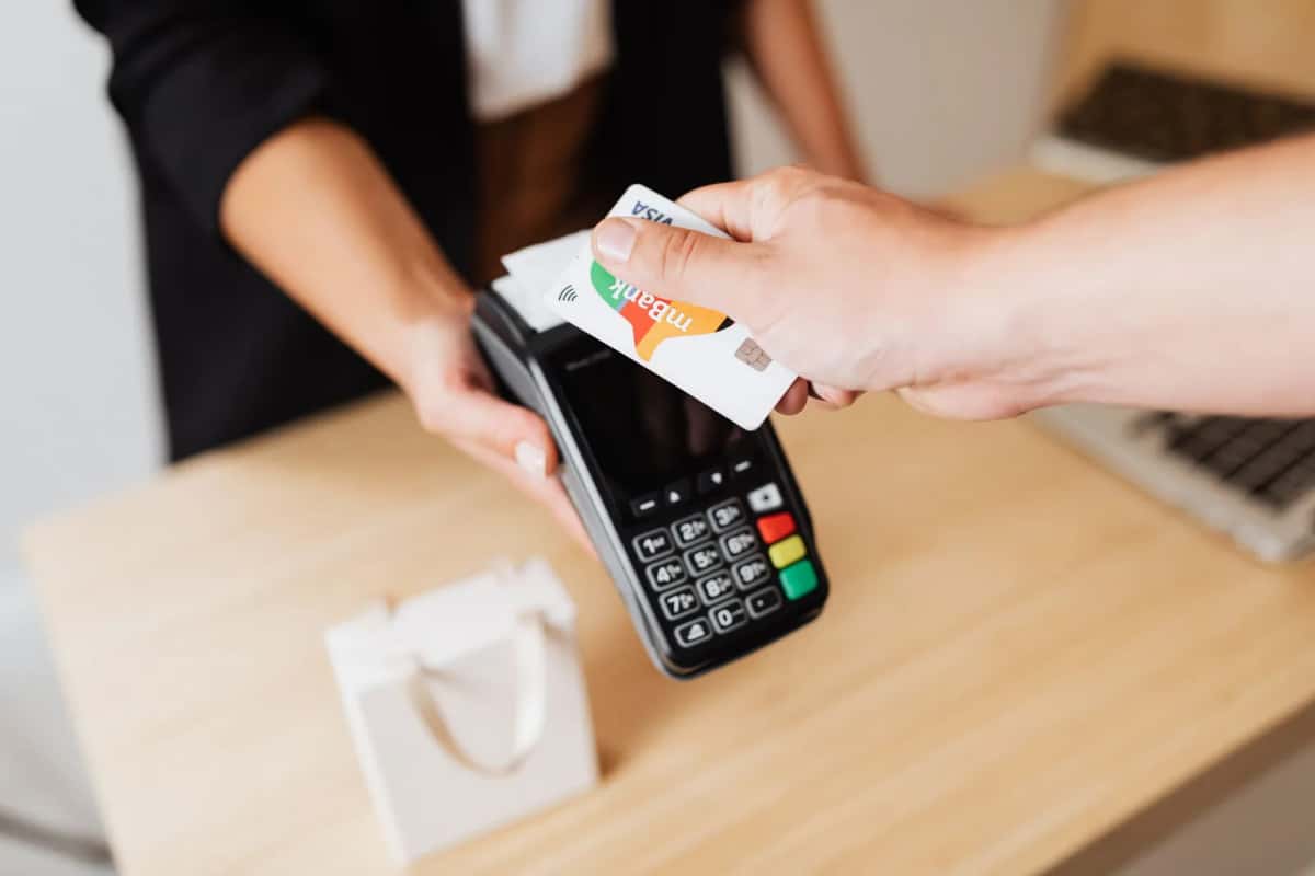 Une main tendant une carte bancaire vers un terminal de paiement sans contact tenu par une commerçante